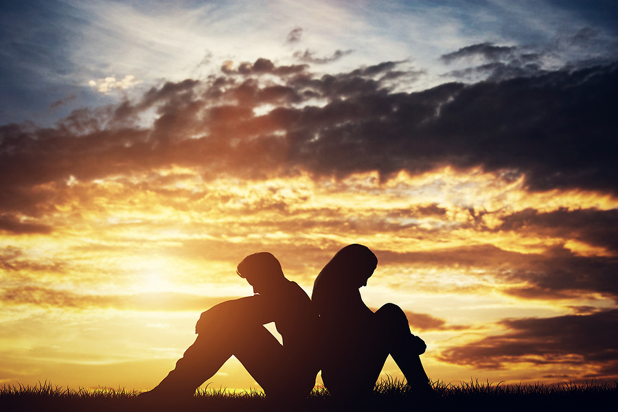 Man and woman sitting back to back at sunset